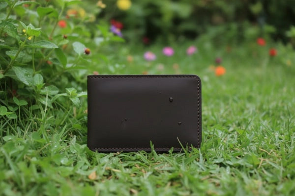 Black leather wallet on grass with flowers in the background